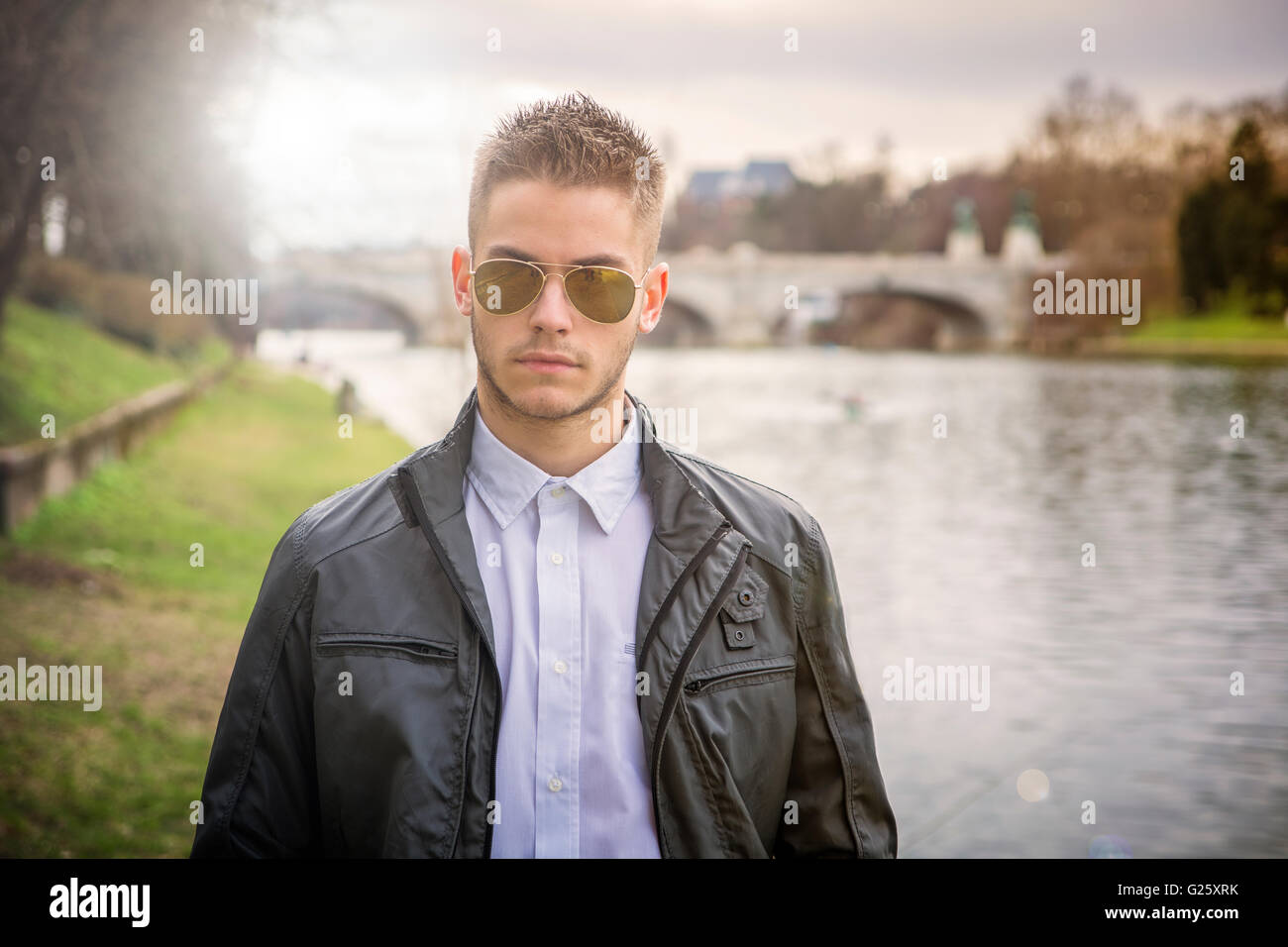 3/4 Länge des kontemplativen leichte Braunhaarige junge Mann trägt graue Jacke und Denim Jeans stehend neben umge Stockfoto