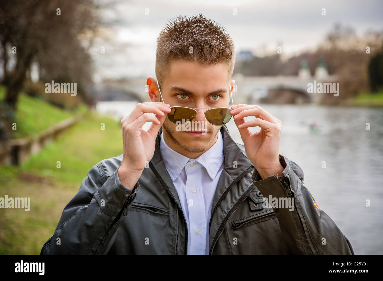 3/4 Länge des kontemplativen leichte Braunhaarige junge Mann trägt graue Jacke und Denim Jeans stehend neben umge Stockfoto