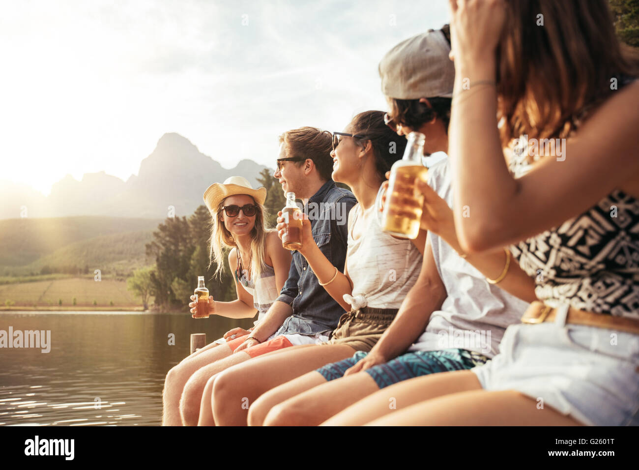 Porträt der jungen Männer und Frauen sitzen an einem Anlegesteg mit Bier. Junge Männer und Frauen, die einen Tag am See zu genießen. Stockfoto