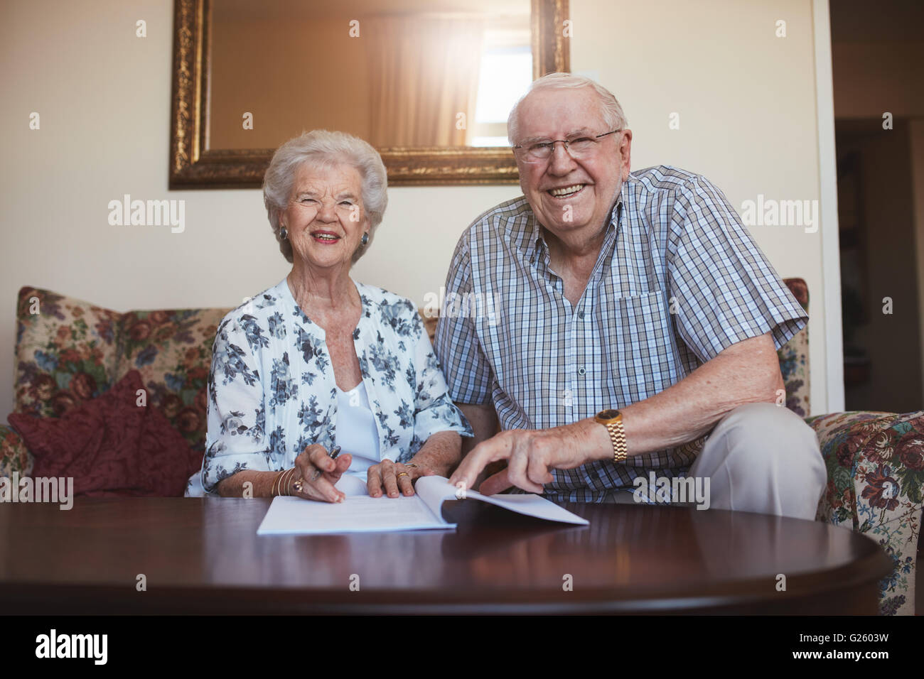 Porträt einer lächelnden Ehepaar im Ruhestand mit Blick auf Dokumente. Senior kaukasischen Mann und Frau auf Sofa im Alter zu Hause sitzen und Stockfoto