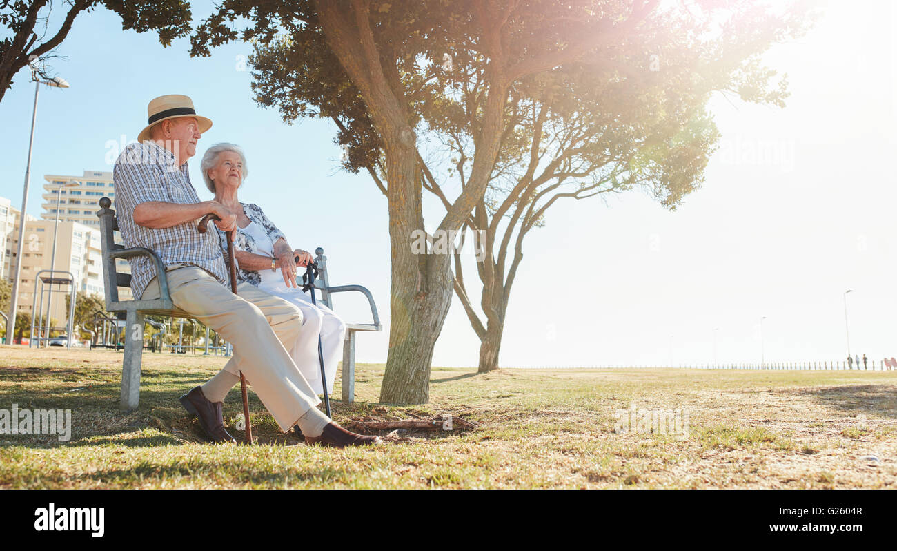 Entspannte älteres Paar an einem sonnigen Tag auf einer Parkbank sitzen. Ältere Mann und Frau im Freien entspannen. Stockfoto