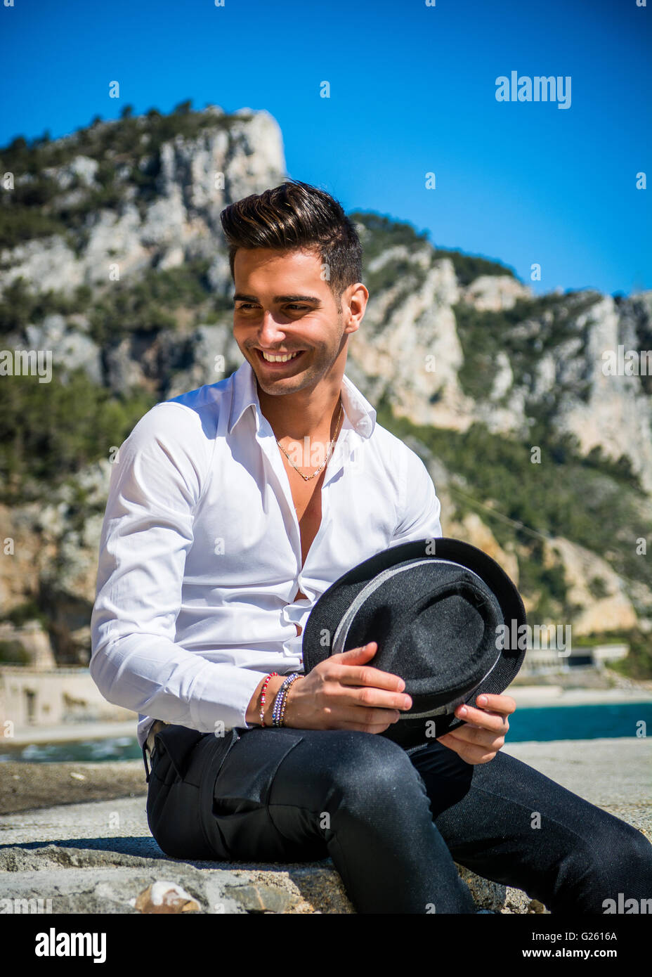 Schönen jungen Mann im klassischen Anzug am Strand halten Sonnenbrille beim wegschauen. Wellen des Meeres im Hintergrund Stockfoto