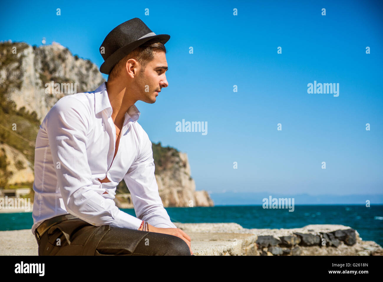 Schönen jungen Mann im klassischen Anzug am Strand halten Sonnenbrille beim wegschauen. Wellen des Meeres im Hintergrund Stockfoto