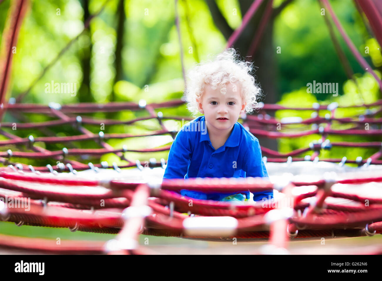 Aktive kleine Kind spielt auf Netz Klettern und springen auf dem Trampolin am Hof Schulhof. Kinder spielen und Klettern im freien Stockfoto
