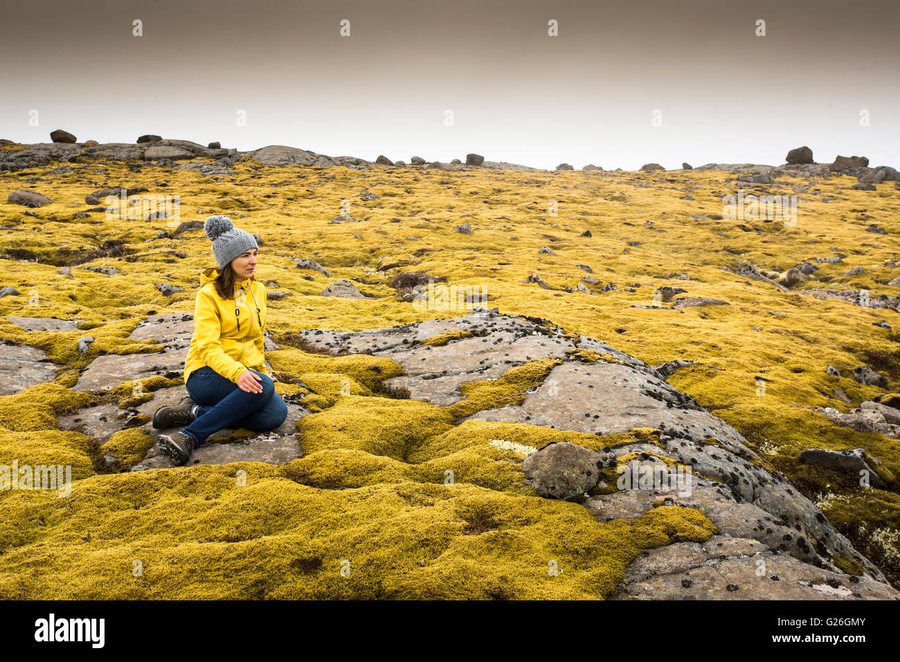 Schöne junge Frau sitzt auf einem Felsen und umgeben von Isländisch Moos Stockfoto