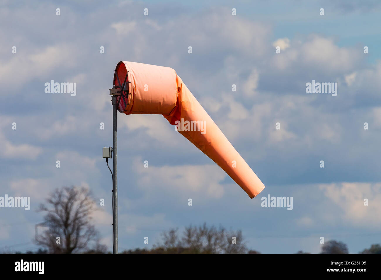 Ein helles orange Windsack zeigt eine leichte Brise vor einem Himmel der Schönwetter-Cumulus-Wolken Stockfoto