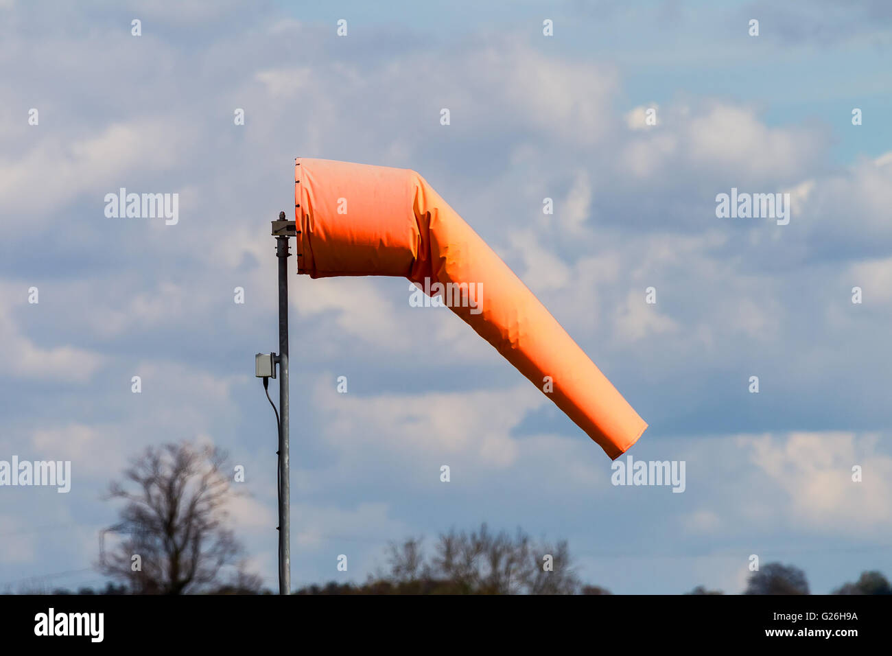 Ein helles orange Windsack zeigt eine leichte Brise vor einem Himmel der Schönwetter-Cumulus-Wolken Stockfoto