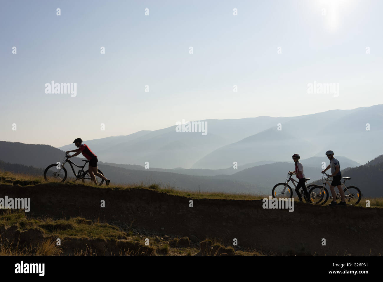 Biker auf dem Berg schieben ihre Räder bergauf bei Sonnenuntergang Stockfoto