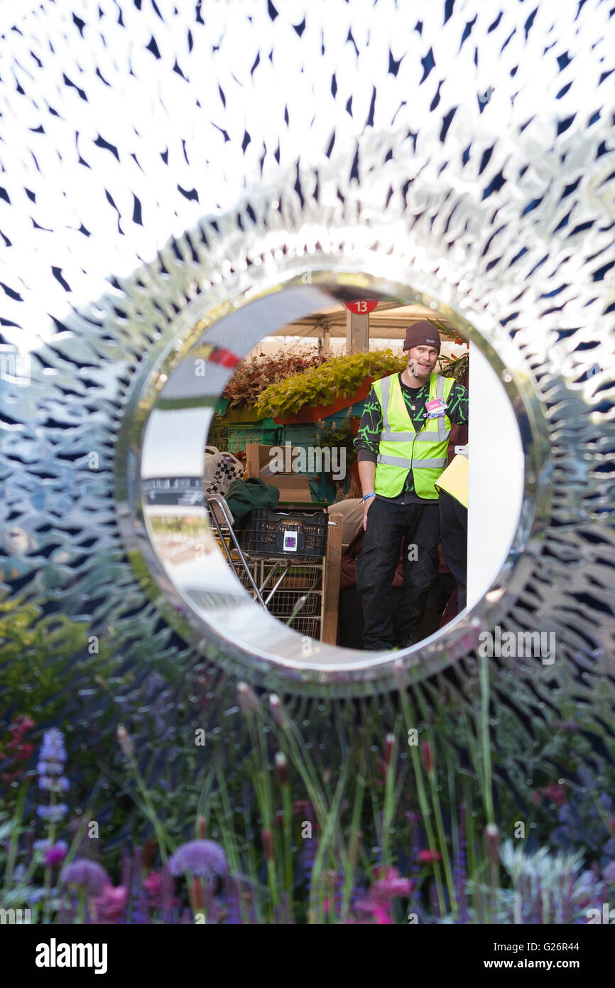 Chelsea Flower Show, London, UK. Arbeiter in einer Leuchtweste durch eine reflektierende Skulptur auf dem David Harber Stand betrachtet. Stockfoto