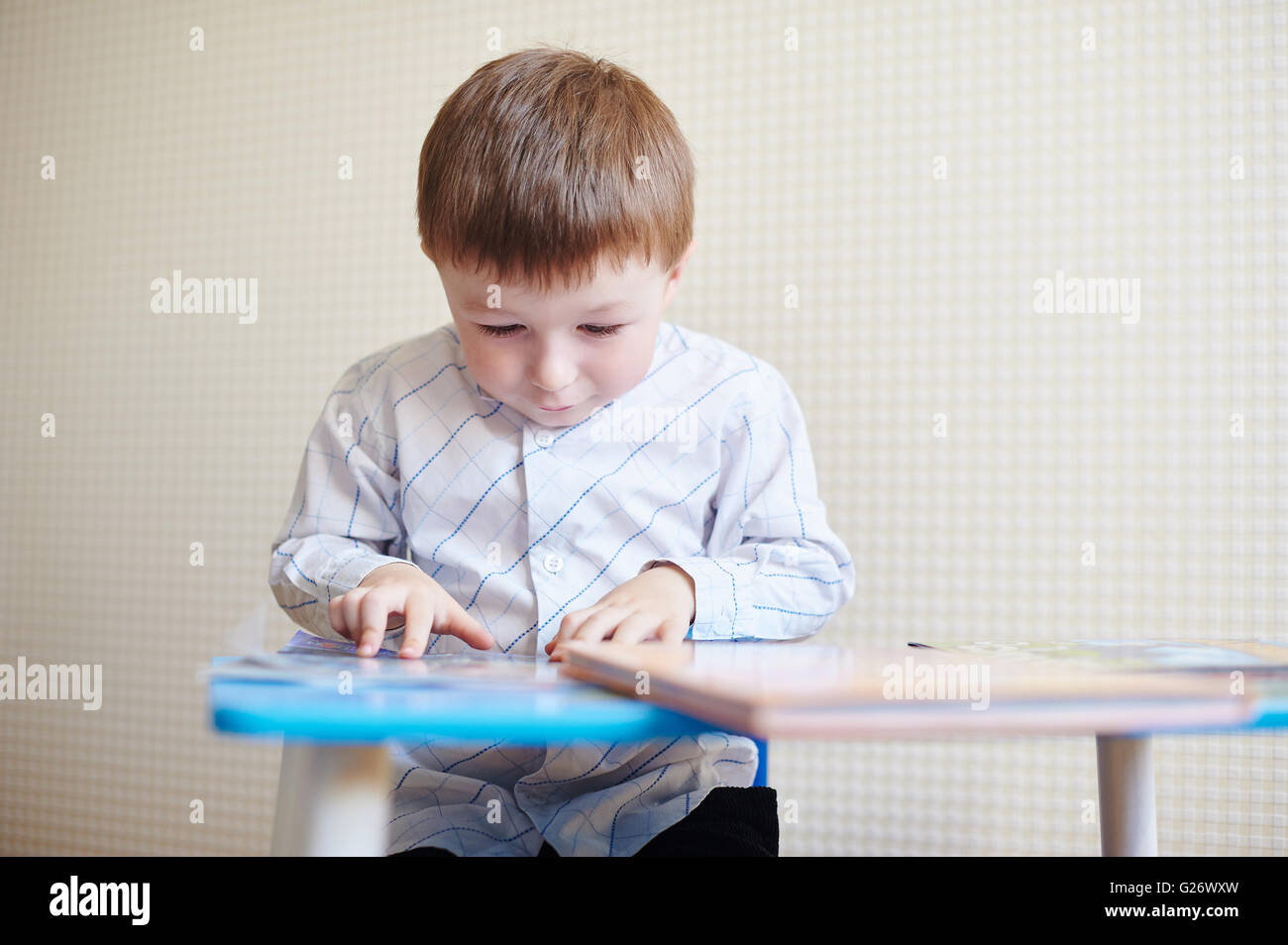 kleiner Junge am Schreibtisch sitzt und liest ein Buch Stockfoto