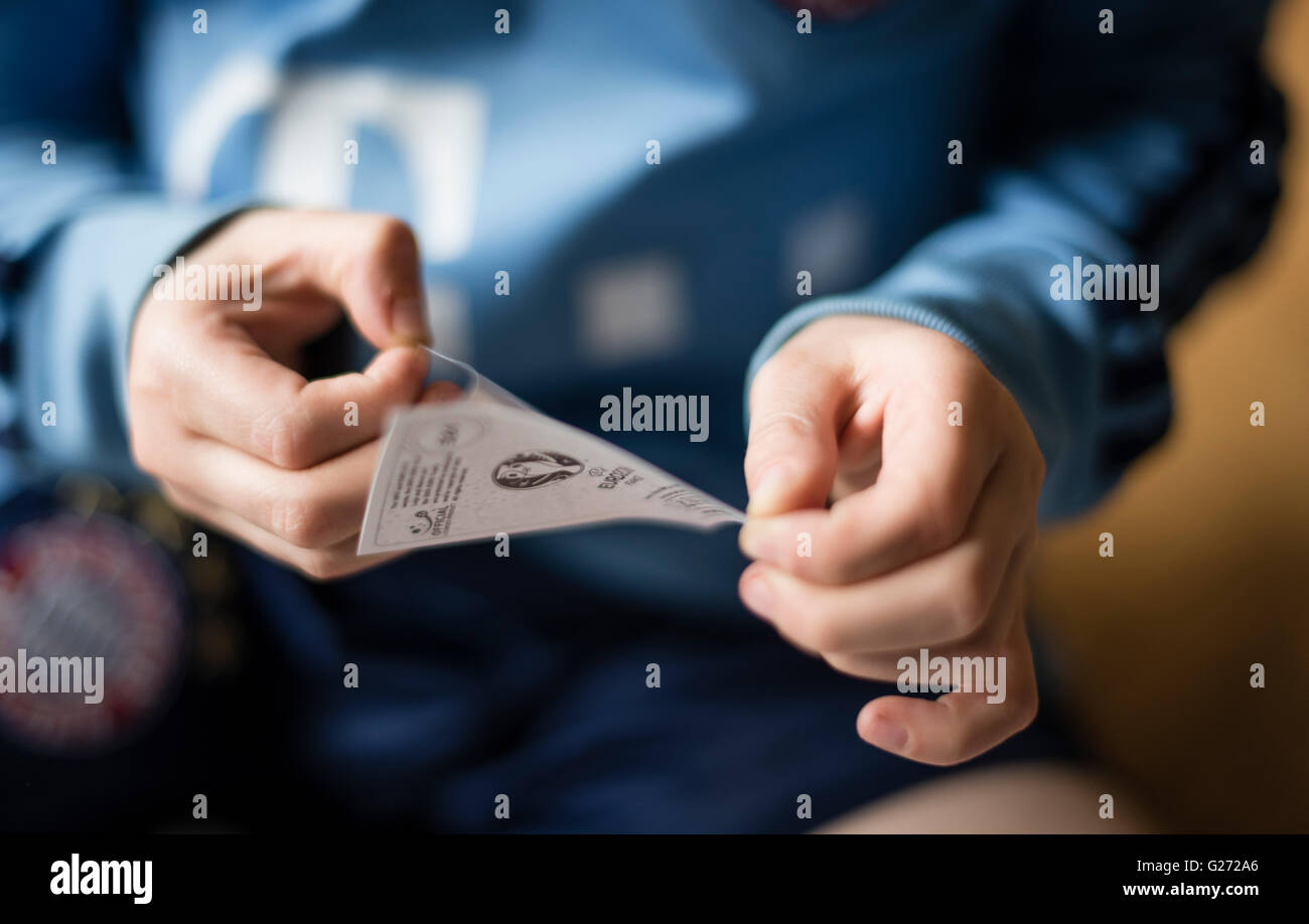 Ein 8 Jahre alter Junge entfernen die Rückseite von einem Panini Fußball Sticker vor dem Einfügen in seinem Aufkleber Sammlung Sammelalbum Stockfoto