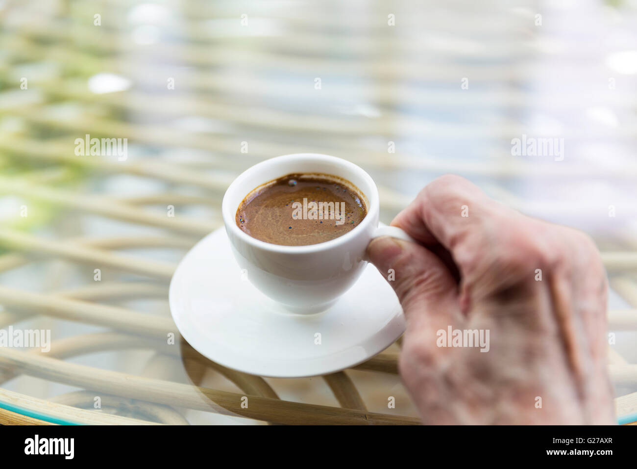 Senior Türkin Hand hält eine Tasse türkischen Kaffee auf einem Glastisch Stockfoto