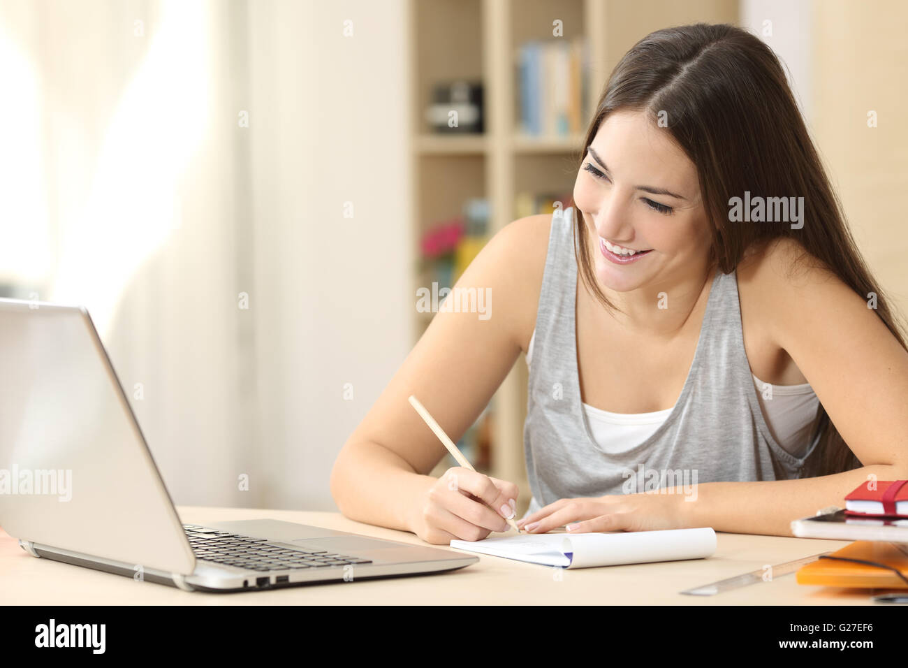 Glückliche Schüler lernen auf Linie und Notizen in einem Notizbuch Hausaufgaben Blick auf Laptop-Bildschirm in einem Schreibtisch zu Hause Stockfoto