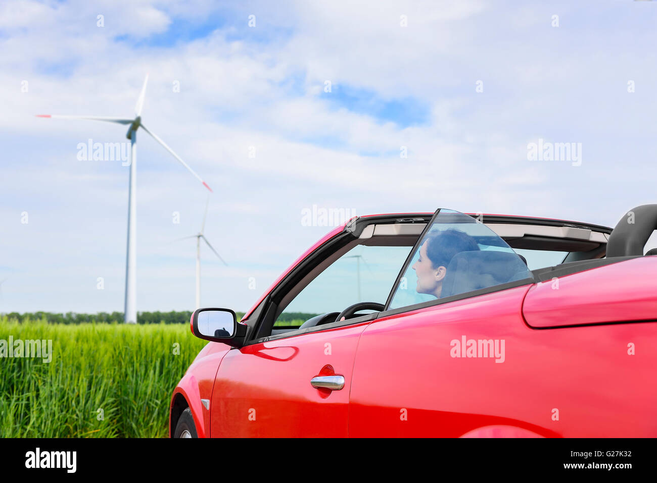 Frau in einem roten Cabrio in einem Feld mit Windkraft. Reisekonzept. Stockfoto
