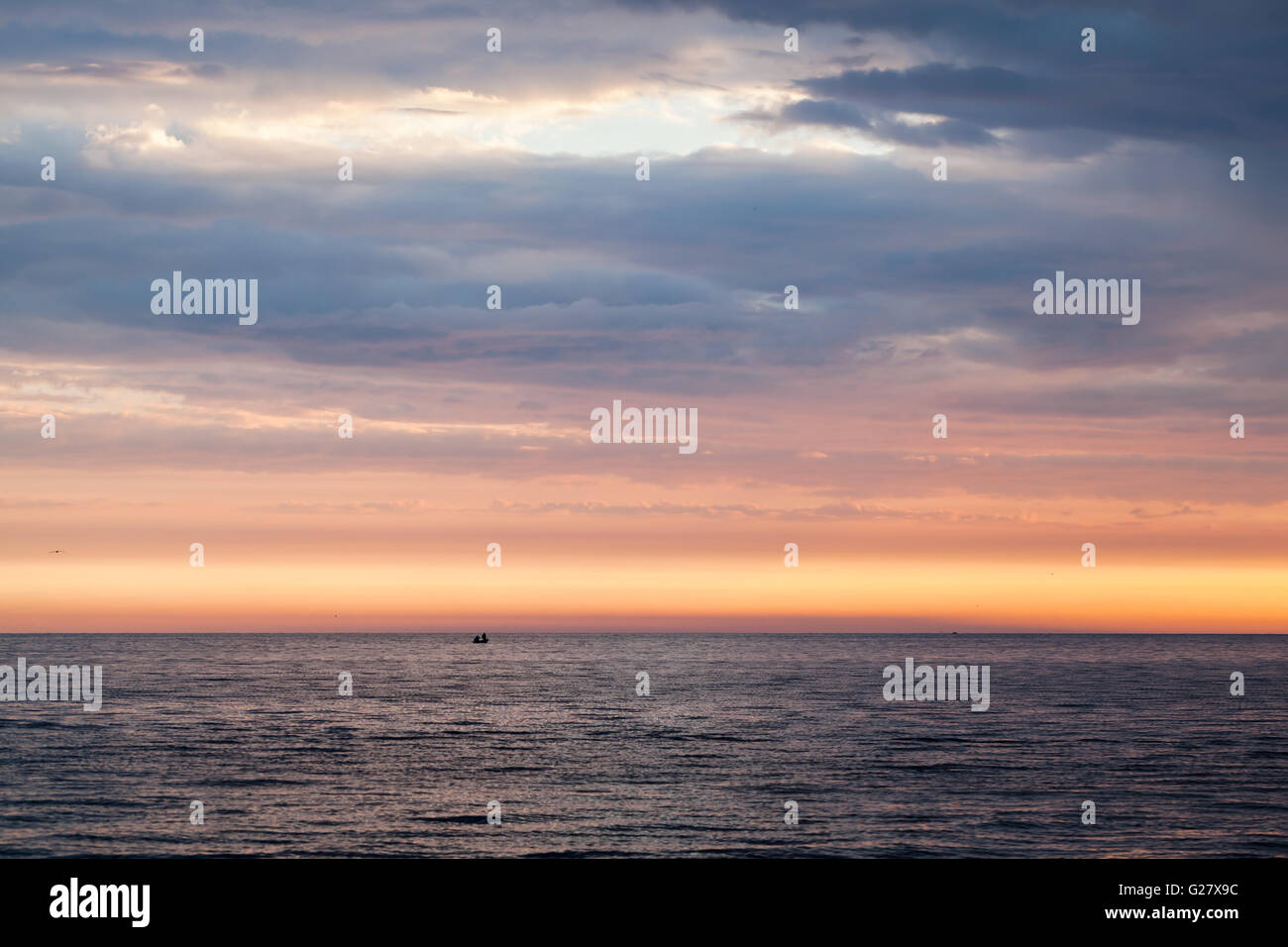 Farbenprächtigen Sonnenuntergang über der Ostsee, bewölkter Himmel, stilles Wasser und Fischer auf einem kleinen Boot in der Ferne Stockfoto