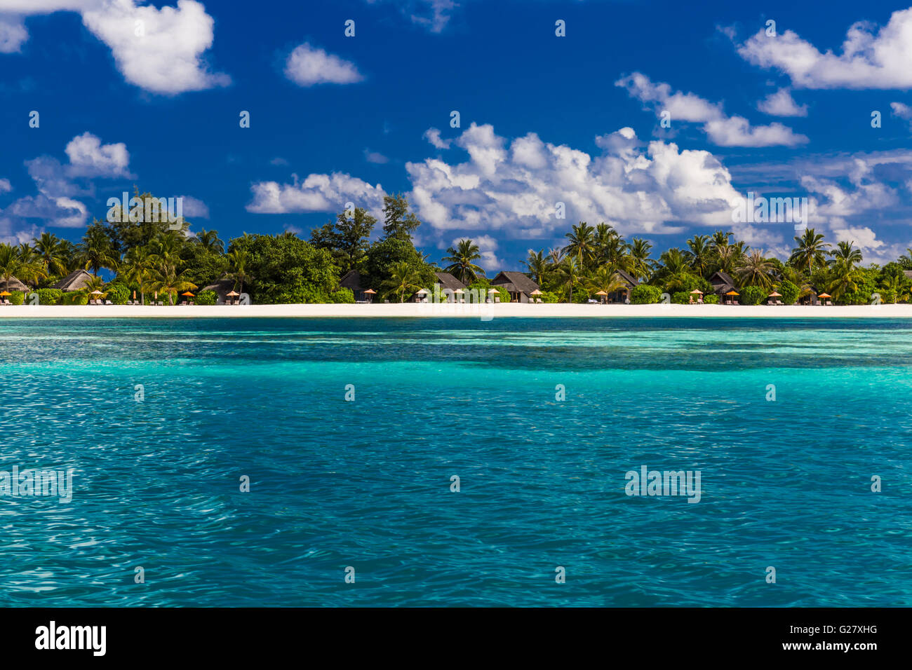 Bungalows auf einer tropischen Insel mit Palmen und lebhaften Strand Stockfoto