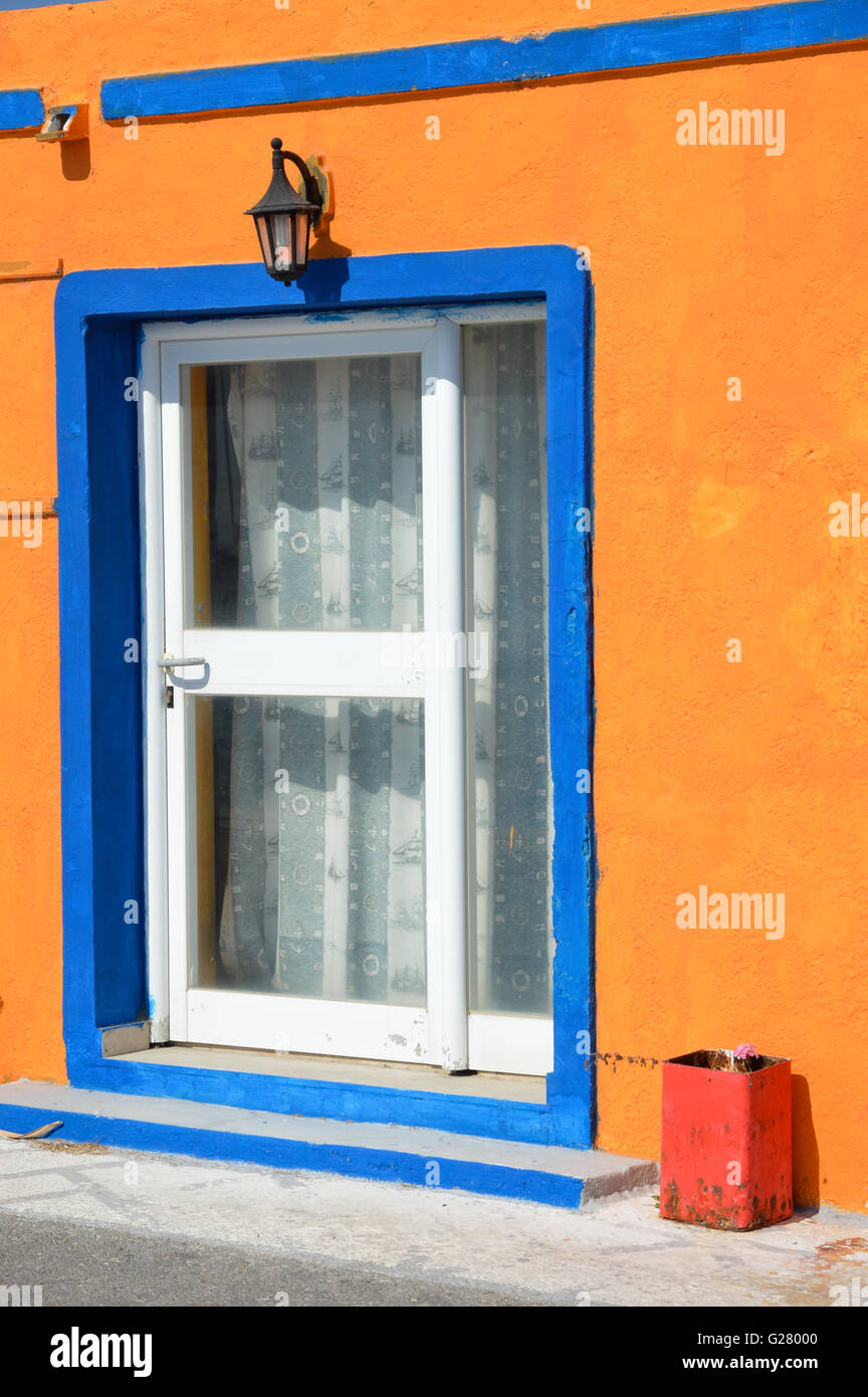 eine weiße glasierte Holz Holz Tür in einen weißen Rahmen mit blauer Kontur fest in eine orange Farbe Render verputzte Wand, Griechenland Stockfoto