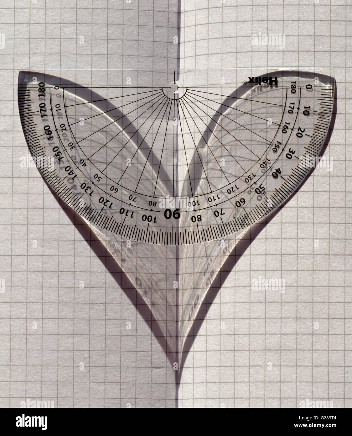 Liebe Mathematik! Ein Winkelmesser im Sonnenlicht auf gefalteten Millimeterpapier, der Schatten ein Herz darstellt. Stockfoto