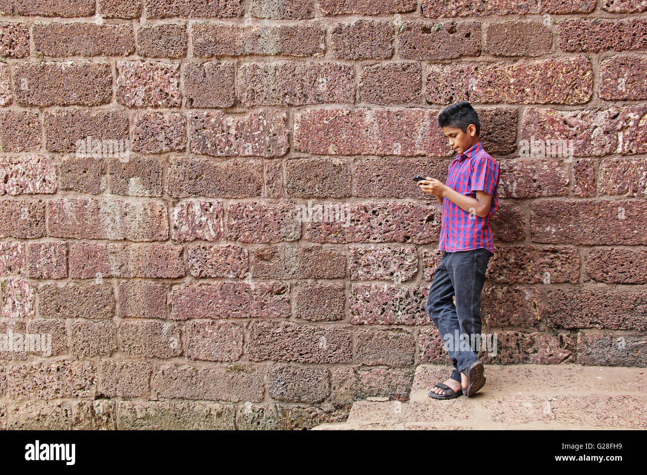 Kluger Junge Mann ernsthaft arbeiten auf Smartphone, roten Ziegelmauer gelehnt Stockfoto