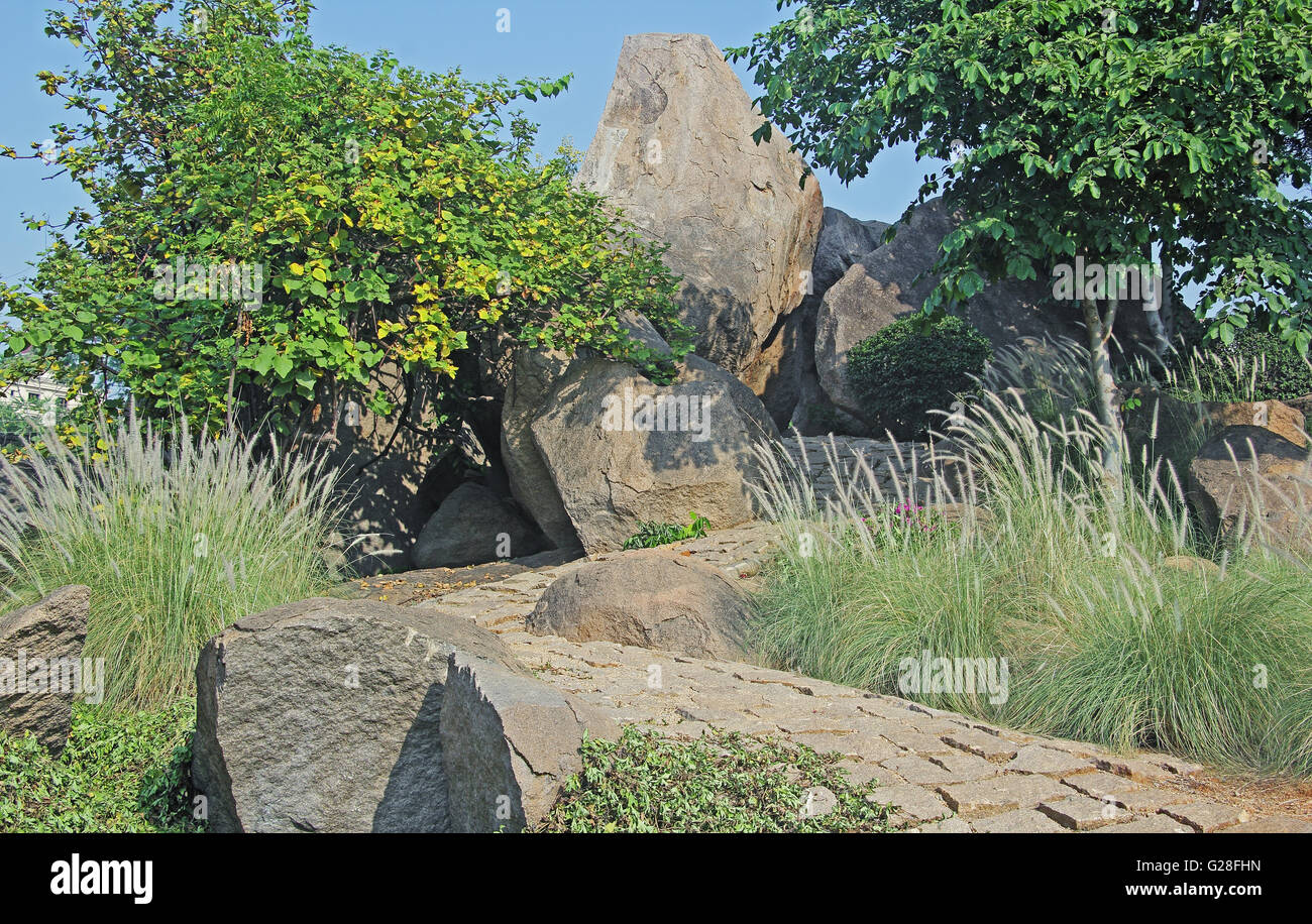 Gewundenen Weg, gepflastert mit grobem Granit Steinplatten, hinauf durch hügeliges Gelände mit riesigen Felsen und Büschen. Stockfoto