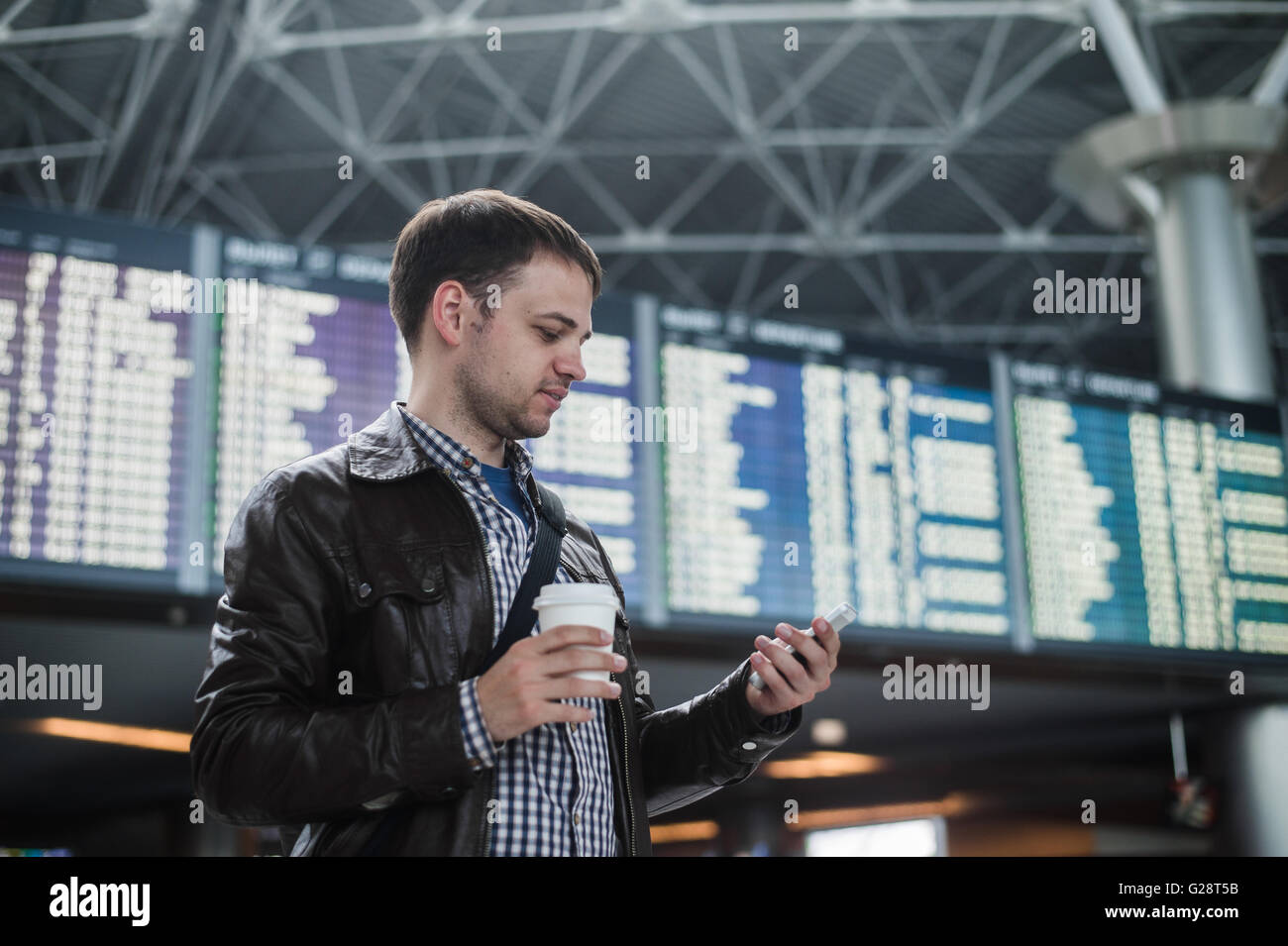 Fröhlicher Mensch mit Kaffee auf dem Handy vor Board Zeitpläne im Flughafen-terminal Stockfoto