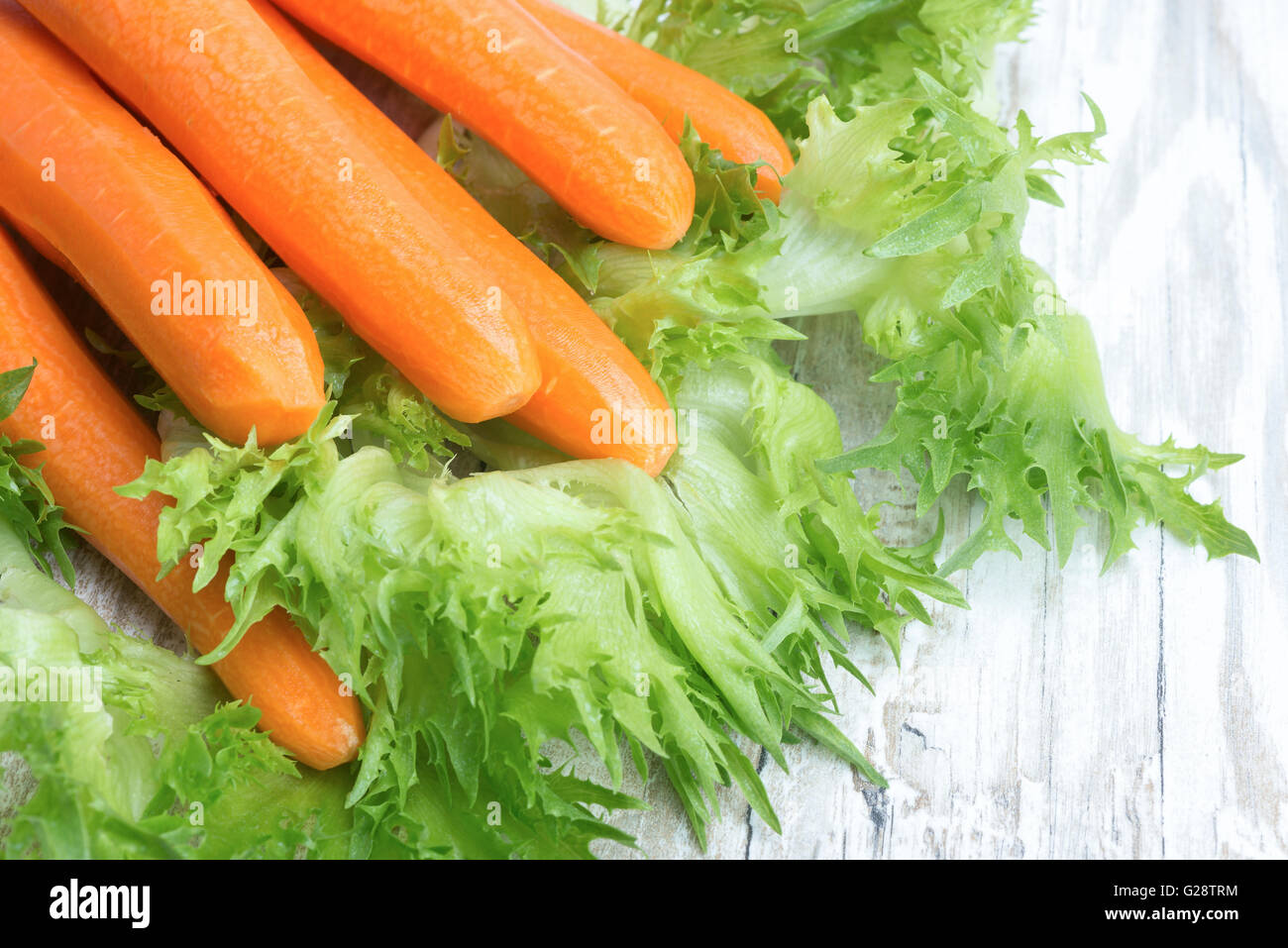 Rohe geschälte Karotten und Salat auf einem Holztisch Stockfoto