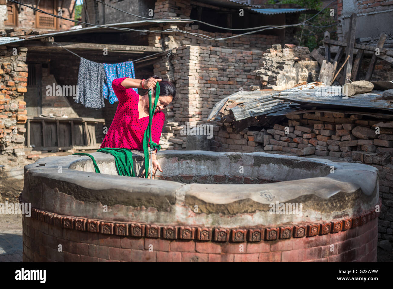 Eine Frau, die Wasser aus einem Brunnen in der alten Nachbarschaft von Bhaktapur, Nepal, zieht. Stockfoto