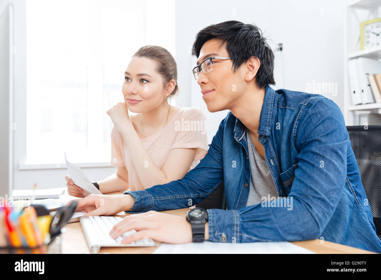 Glückliche junge Frau und asiatischer Mann in Glaases mit Computer zusammen zu arbeiten Stockfoto