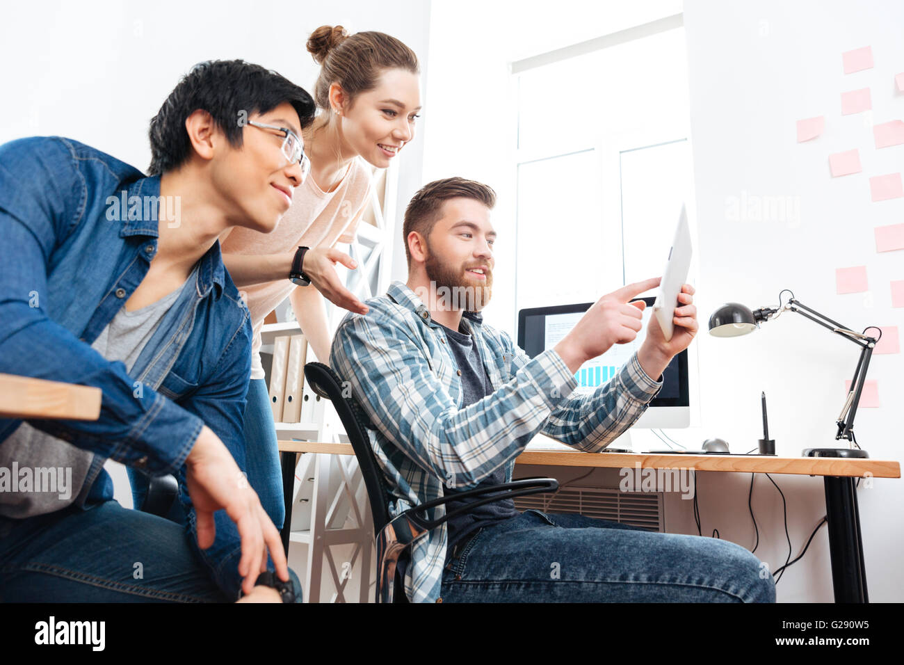 Drei glückliche junge Geschäftsleute arbeiten und mit tablet im Büro Stockfoto