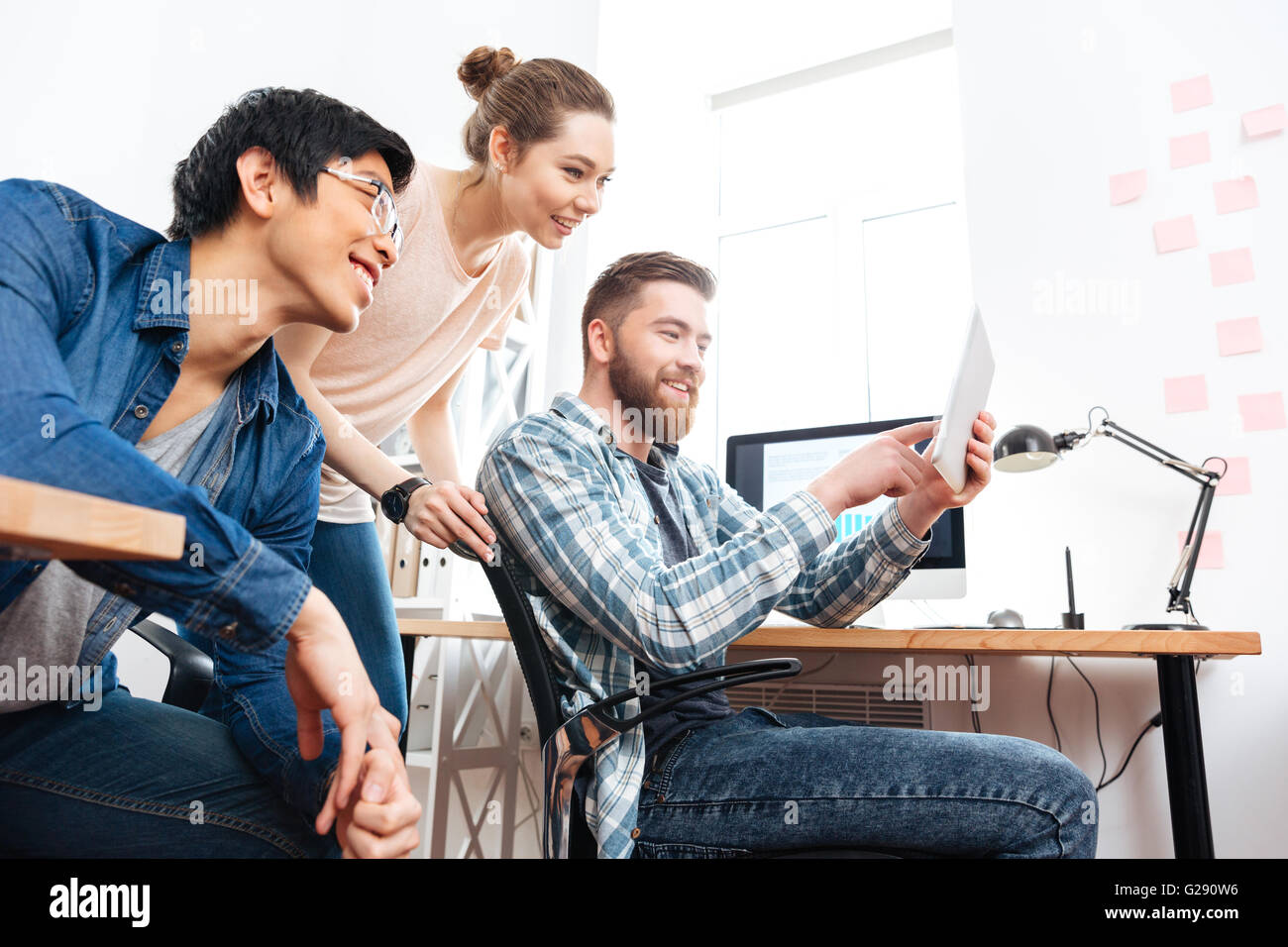 Drei lächelnde junge Geschäftsleute arbeiten mit Tablet-PC im Büro Stockfoto