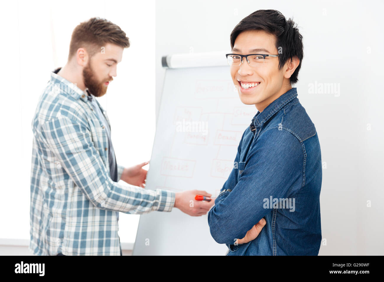Lächelnder junge asiatische Mann arbeitet mit seinem Kollegen mit flipchart Stockfoto