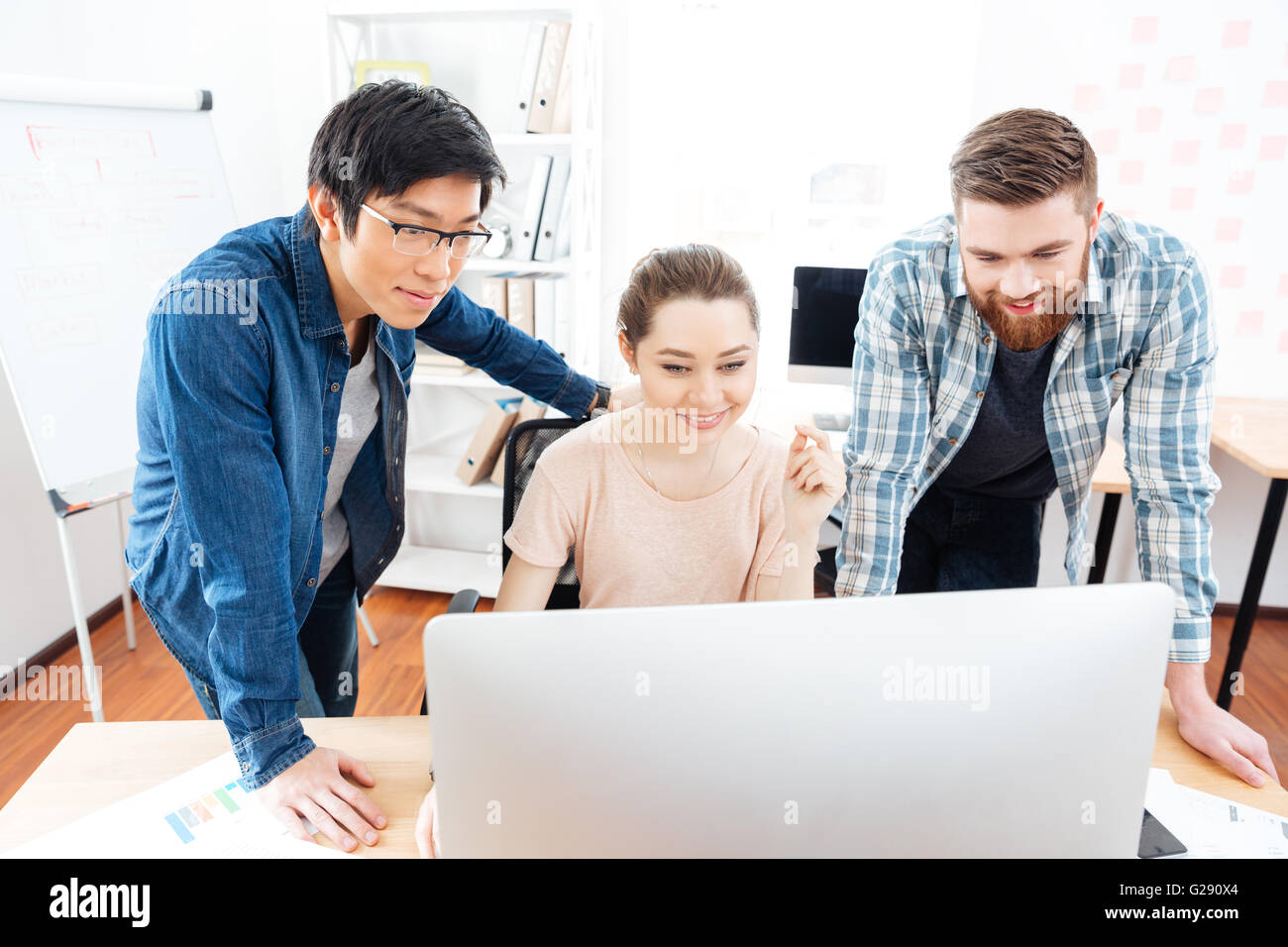 Lächelnde junge Frau und zwei schöne Männer mit Computer im Büro zusammen zu arbeiten Stockfoto