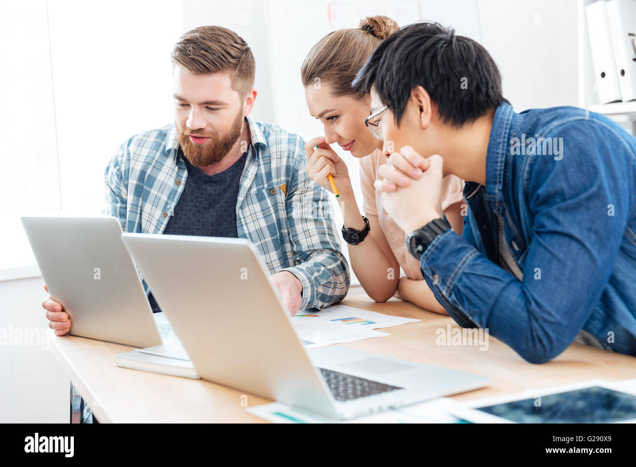 Drei junge Geschäftsleute, die für das Projekt mit Laptops im Büro zusammen arbeiten Stockfoto