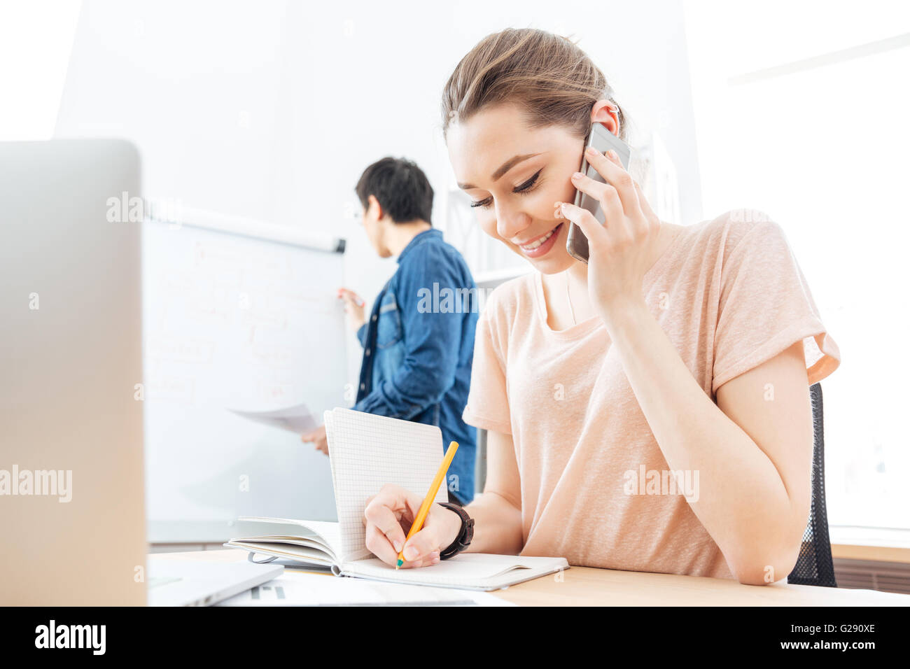 Fröhliche junge Frau am Handy während ihrer Kollegin mit Flipchart in office Stockfoto