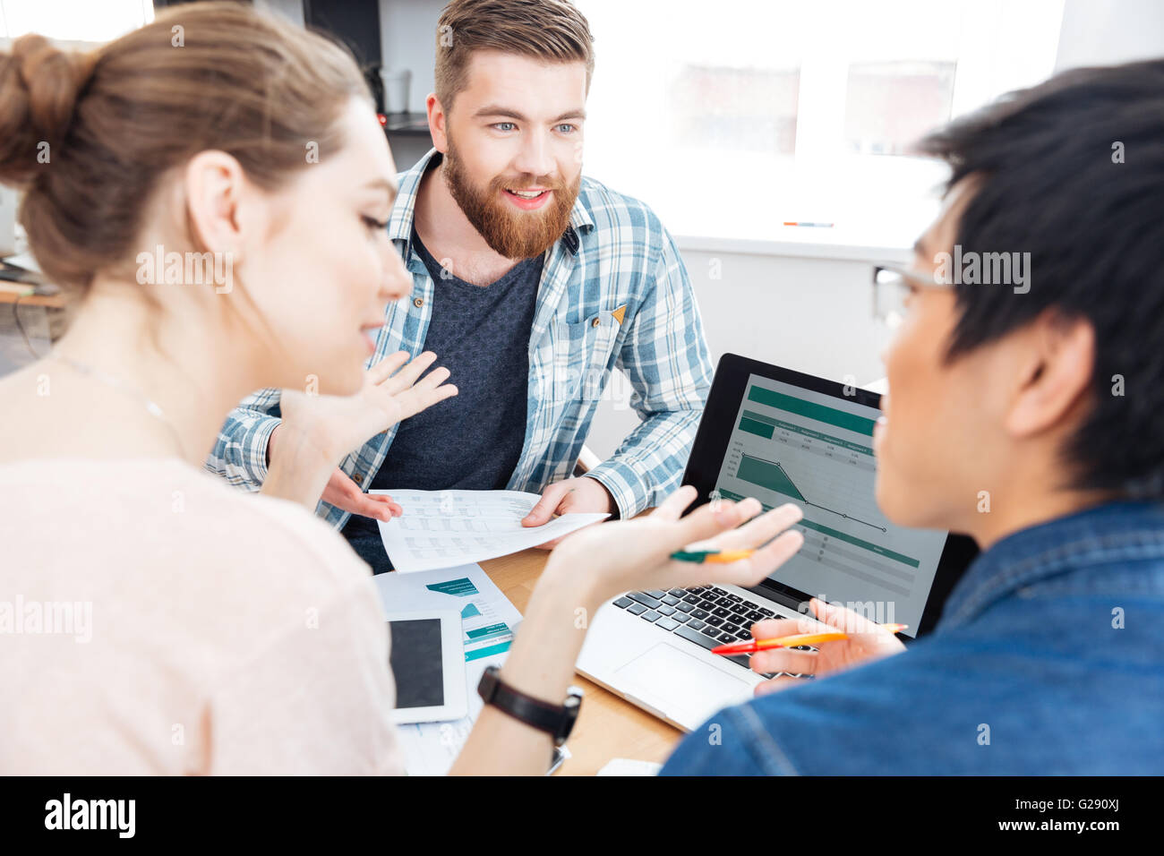 Drei glückliche junge Unternehmer arbeiten und diskutieren Businessplan im Büro Stockfoto