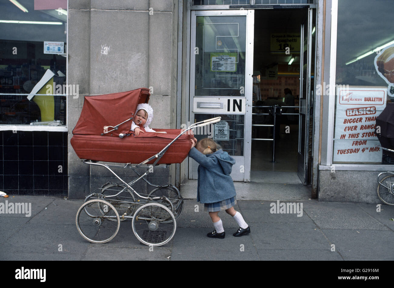 Archiv-Bild des Babys im Kinderwagen vor einem Geschäft mit Schwester Kleinkind 1970 Stockfoto