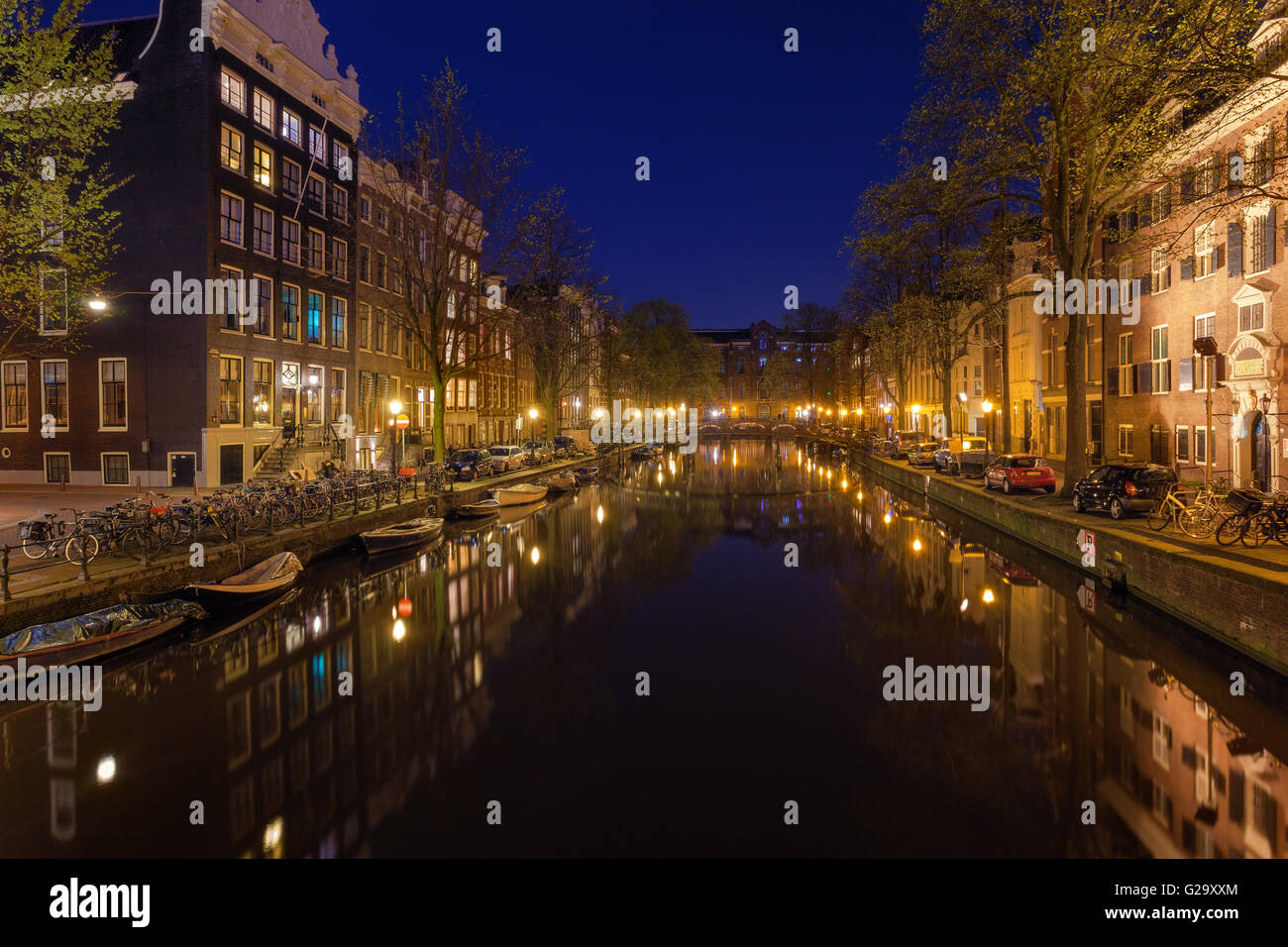 Schöne Nacht Stadtbild mit traditionellen alten Häusern in Amsterdam, Niederlande. Die Lichter der Stadt in Wasser mit blauer Himmel wider. Stockfoto