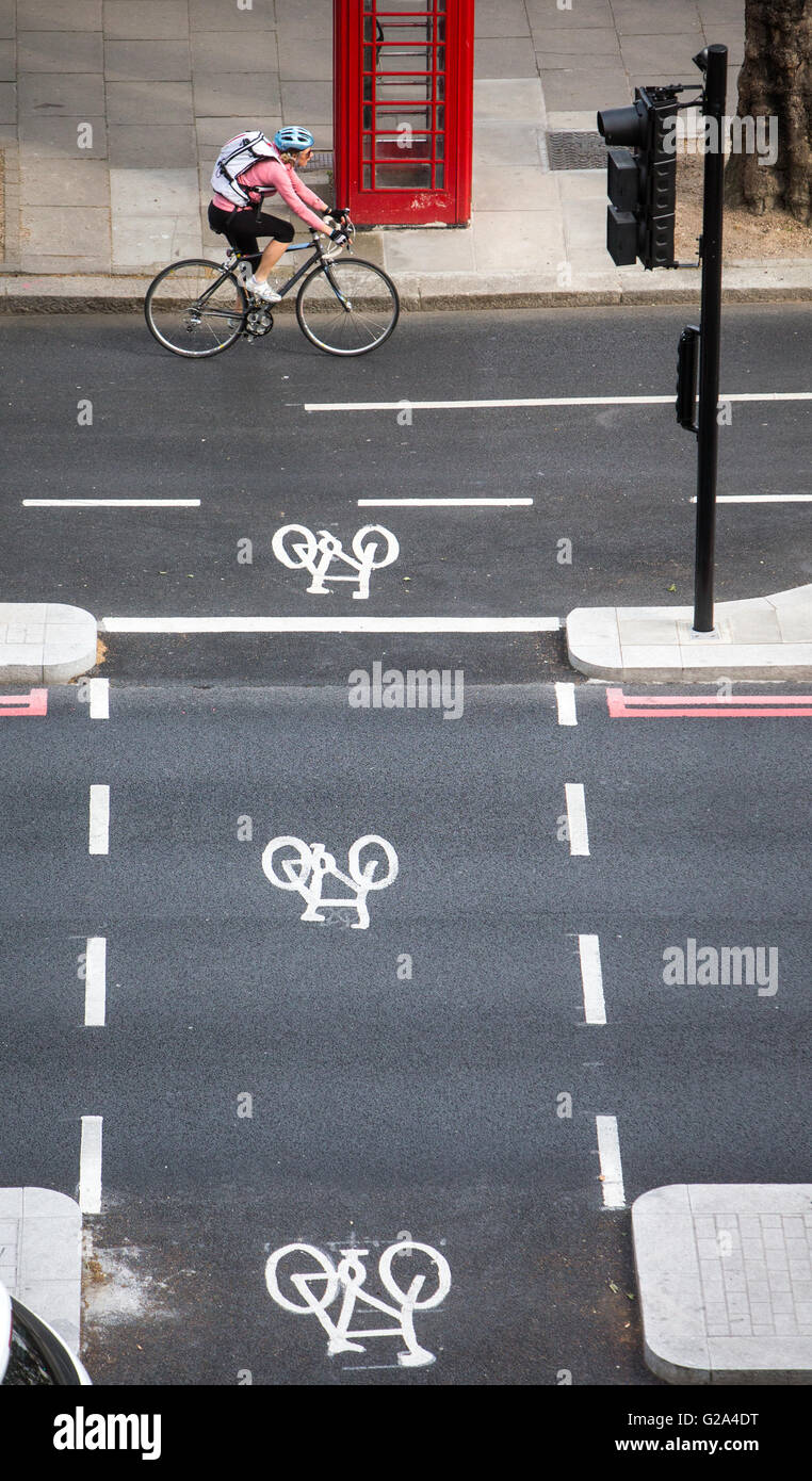 Eine Luftaufnahme eines Radfahrers in ein Radweg vorbei an eine rote Telefonzelle mit drei Zyklus-Zeichen auf dem Damm in London Stockfoto