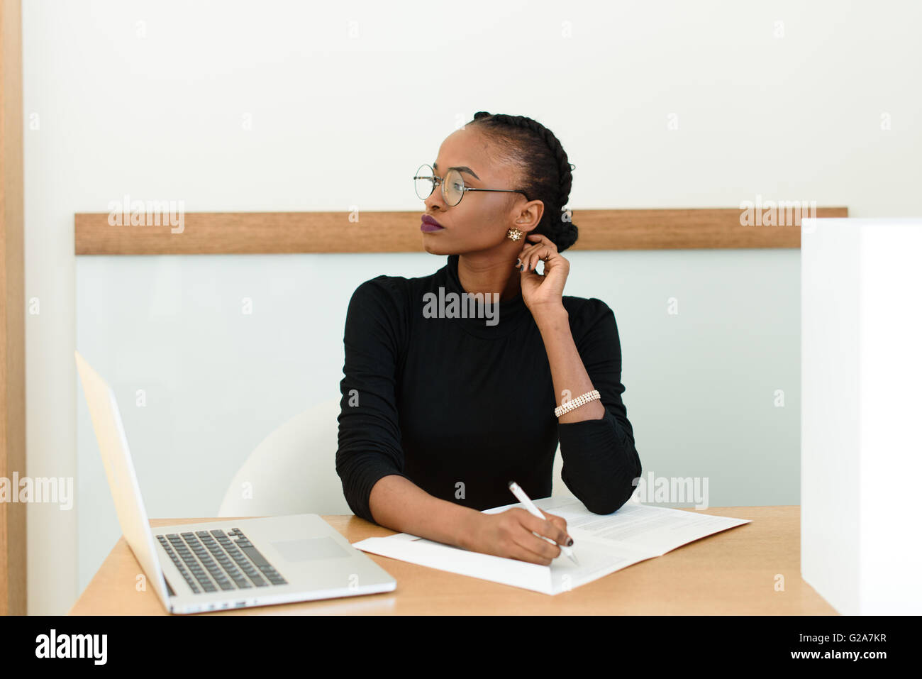 Nachdenklich schwarz Geschäftsfrau in Gläsern berühren ihren Hals Wegschauen am Schreibtisch mit Notizblock und Laptop im Büro Stockfoto