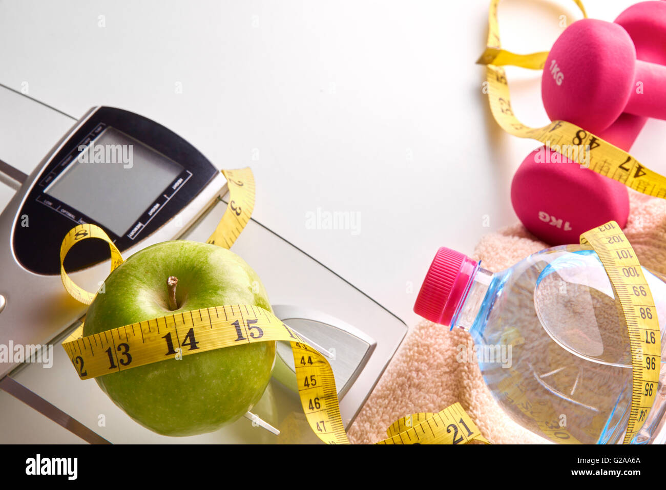 Skala, rosa Hanteln mit Apfel, Mineralwasserflasche, Handtuch und Maßband auf weißen Tisch. Konzept-Gesundheit, Ernährung, Ernährung eine Stockfoto