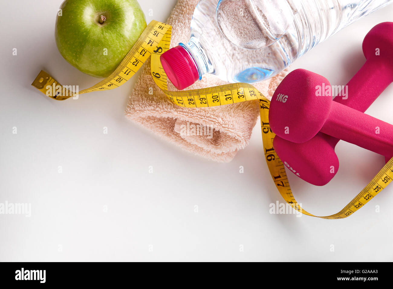 Rosa Hanteln mit Apfel, Mineralwasserflasche, Handtuch und Maßband auf weißen Tisch. Konzept-Gesundheit, Ernährung und Sport. Stockfoto