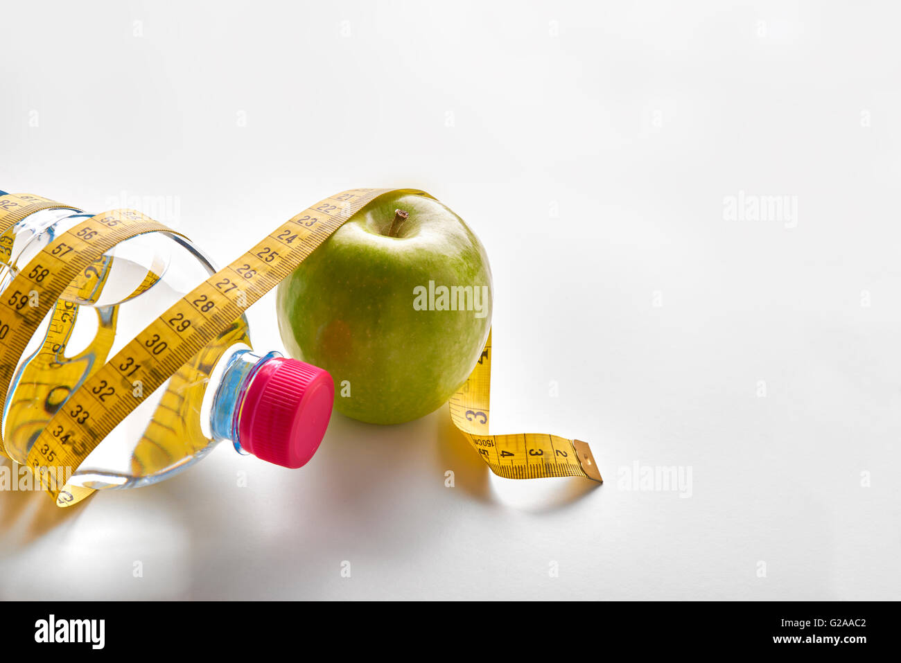 Maßband um eine Flasche Mineralwasser und Apfel auf weißen Tisch. Konzept Gesundheit, Diät und Ernährung. Horizontale Stockfoto