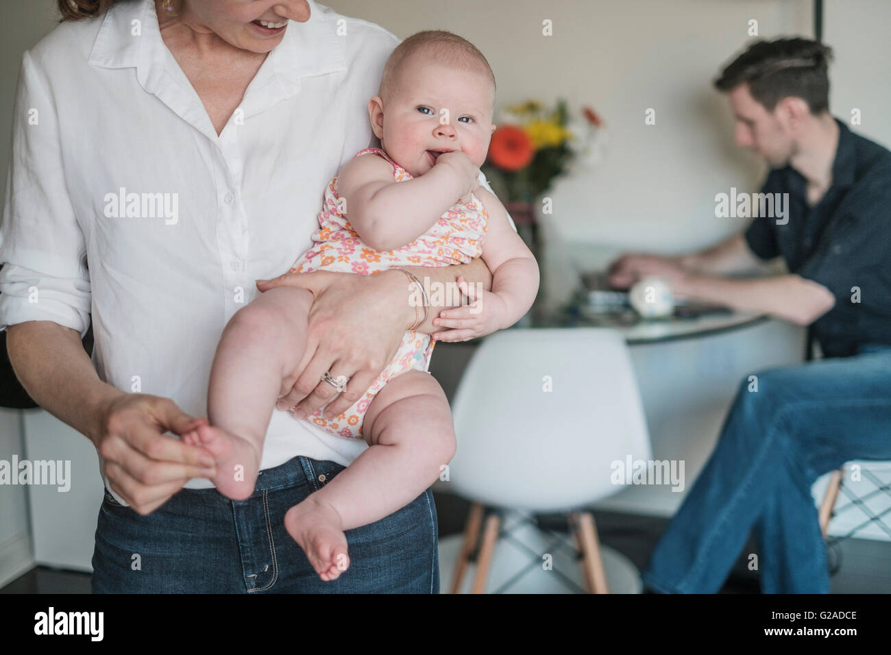 Mutter mit Kind (2 bis 5 Monate) und Vater arbeitet im Hintergrund Stockfoto