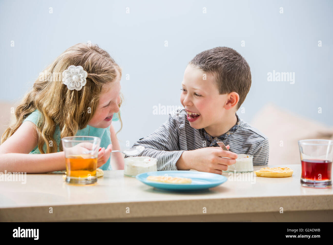 Lächelnde Kinder (6-7, 8-9) Essen Pudding am Tisch Stockfoto