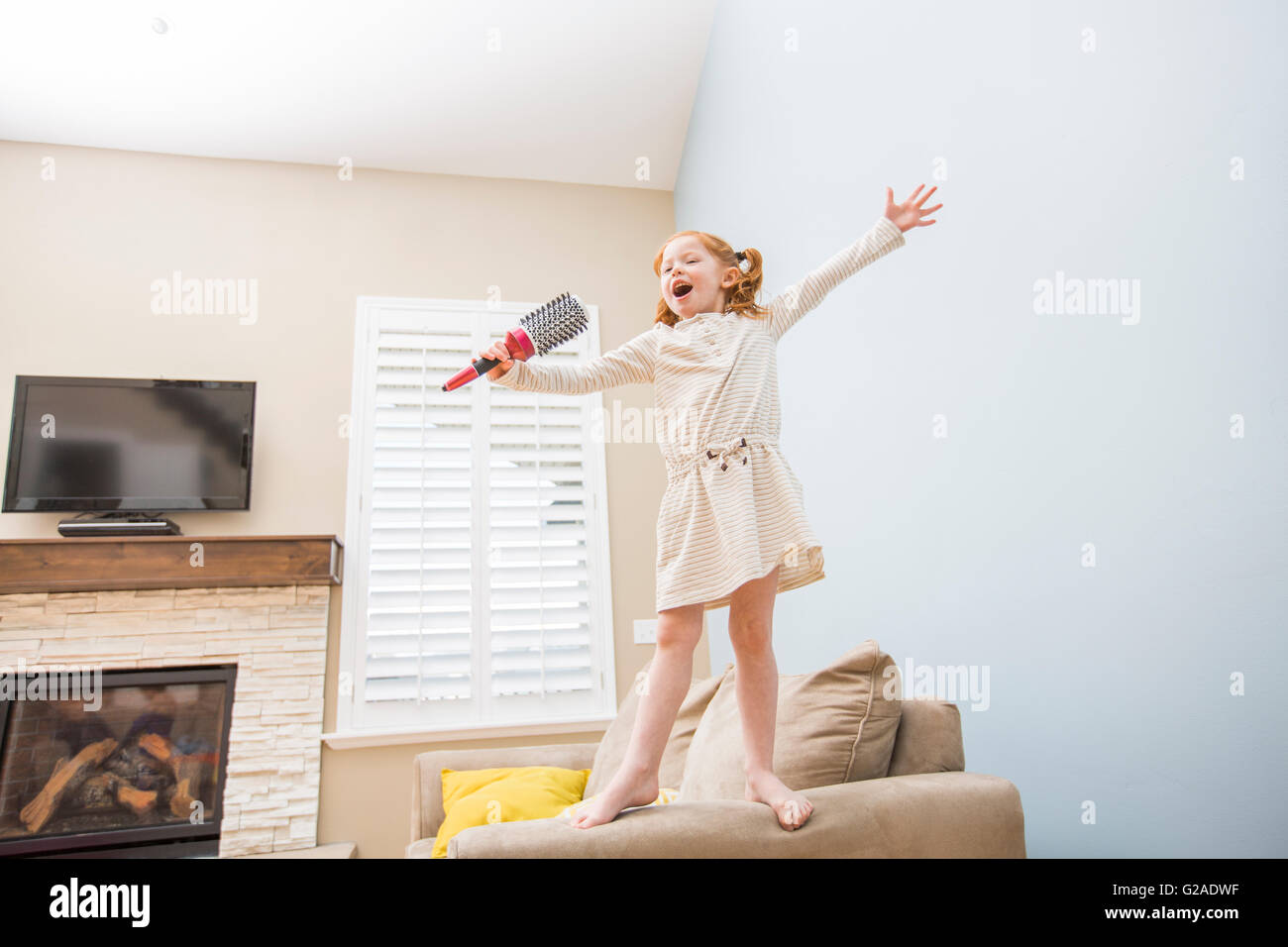 Kleines Mädchen (4-5) singt in der Haarbürste auf sofa Stockfoto