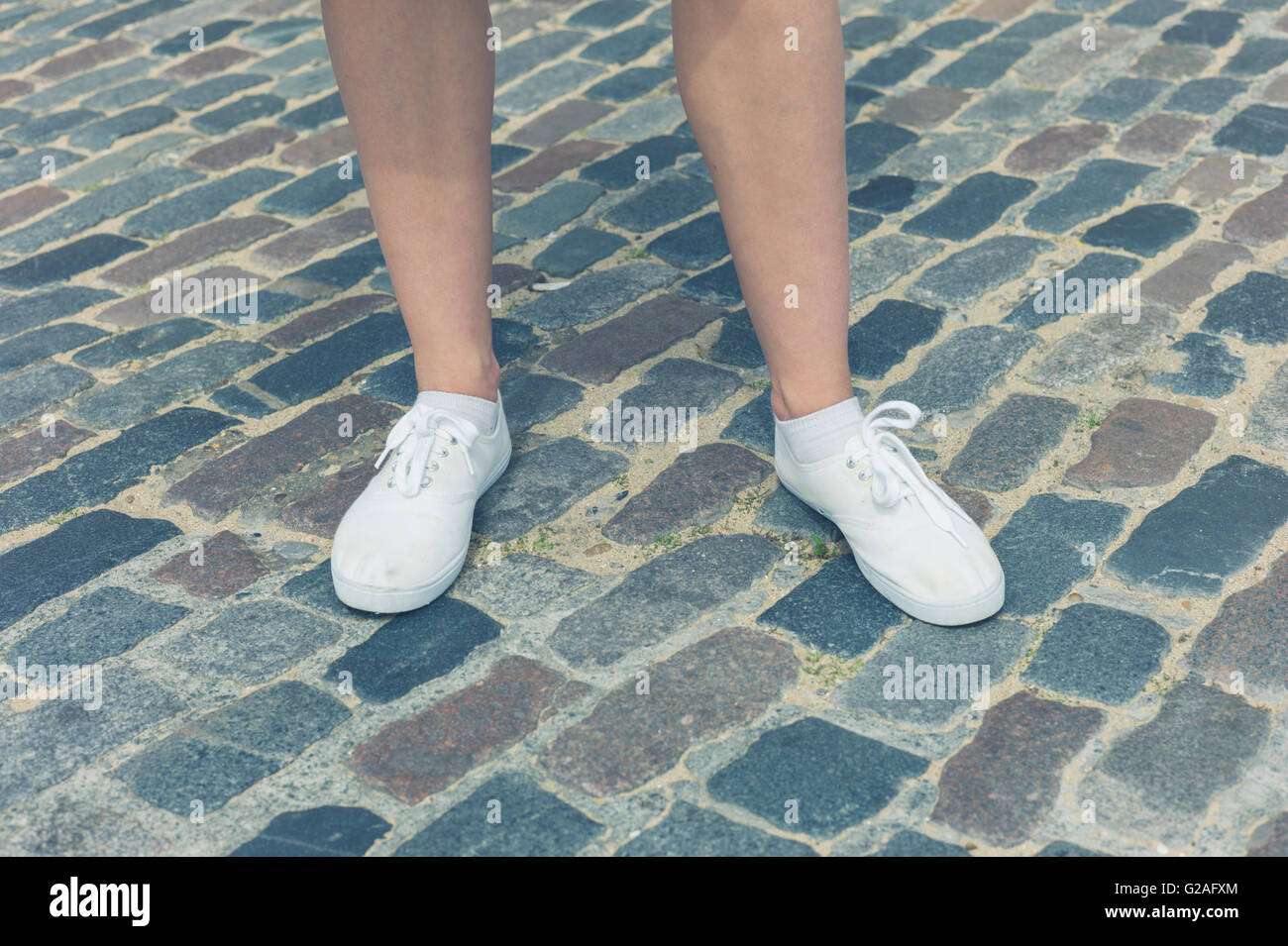 Die Beine und Füße einer jungen Frau, stehend auf einem gepflasterten stret Stockfoto