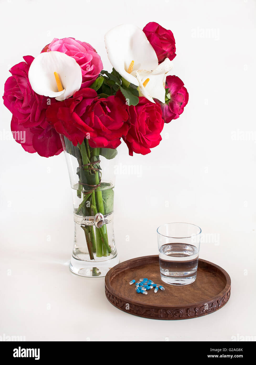 Glas Wasser, Medikamente, Blumen und Tablett aus Holz Stockfoto