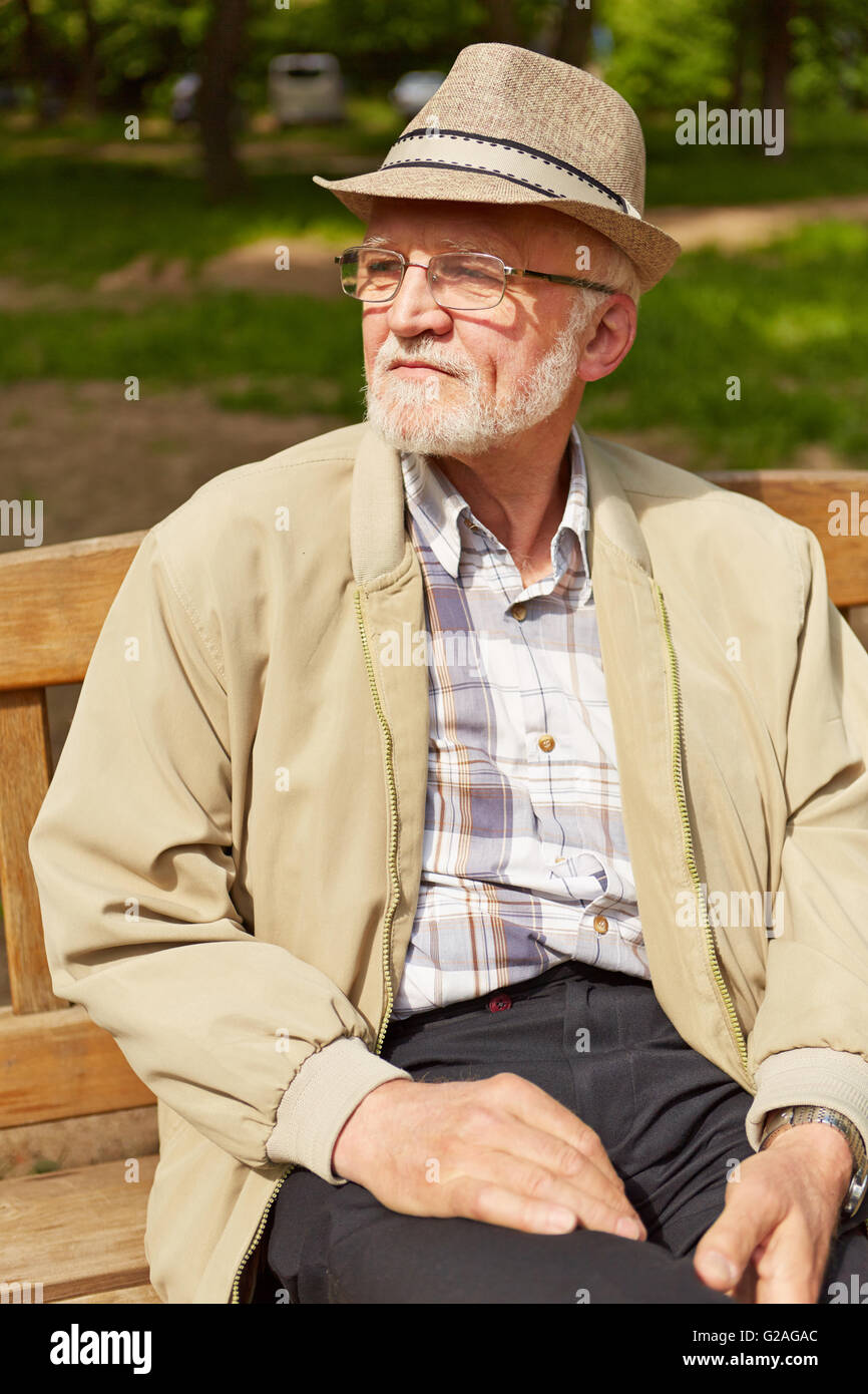 Alter Mann mit Hut und Brille sitzt auf der Parkbank im Sommer Stockfoto
