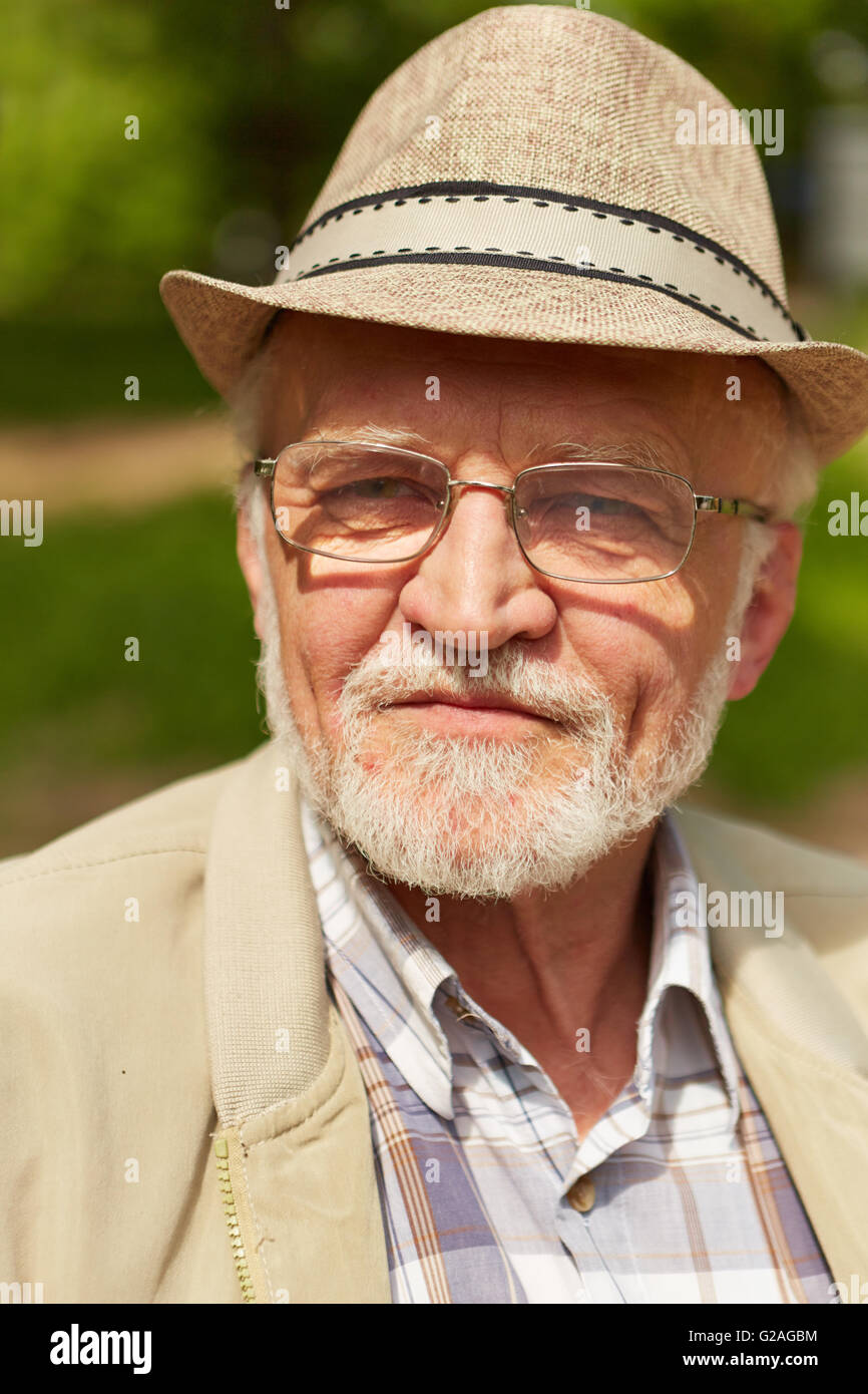 Nachdenklich Alter Mann mit Hut und Brille sitzt in einem Park im Herbst Stockfoto
