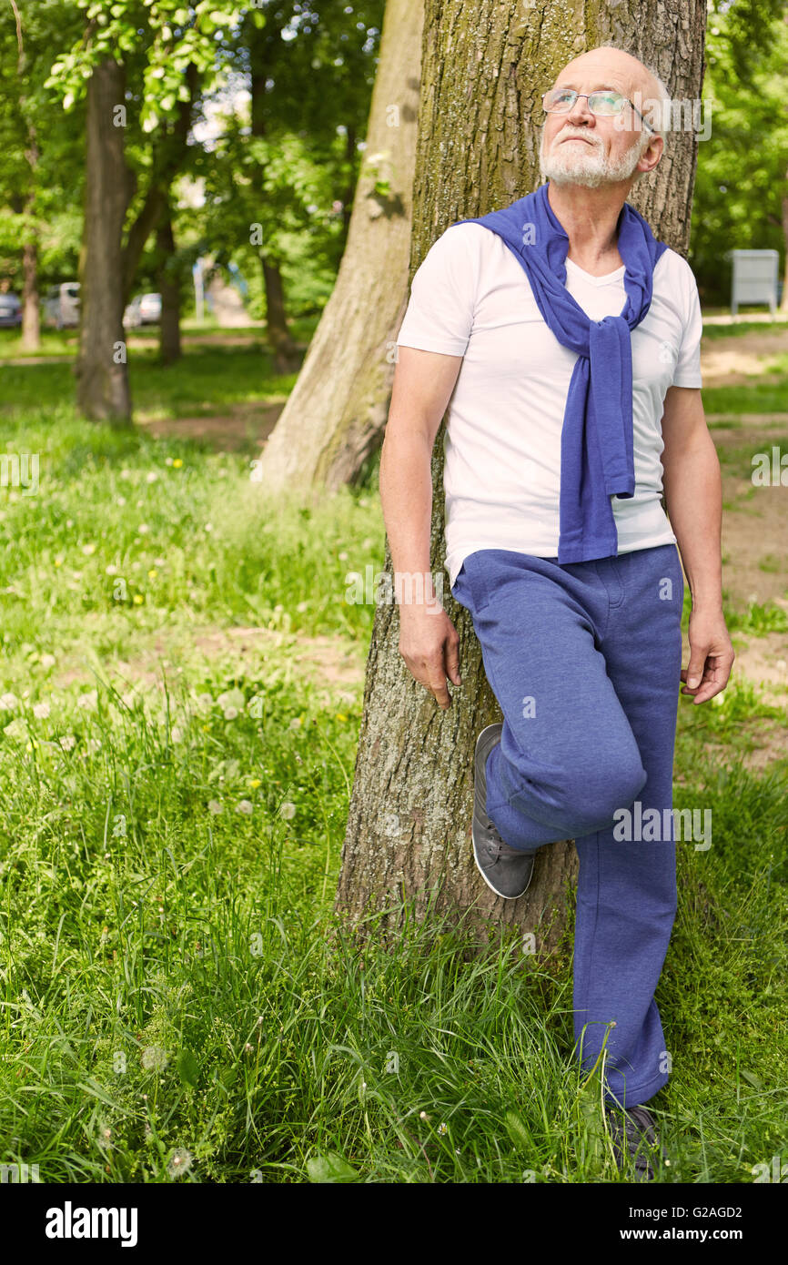 Nachdenklich Greis stützte sich auf einen Baum in einem Park im Sommer Stockfoto